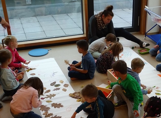 Kinder kleben getrocknete Blätter auf Papierbahnen